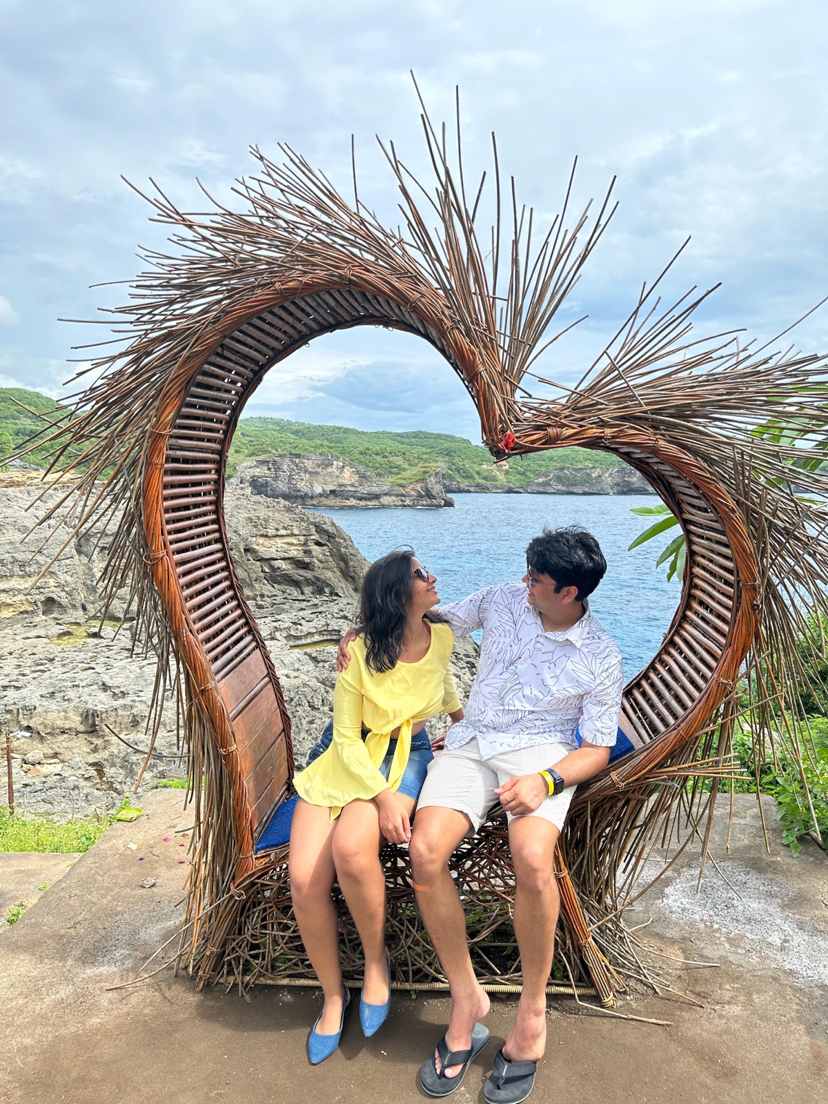 Priyam and Manish sitting in a heart-shaped wooden seat overlooking the sea