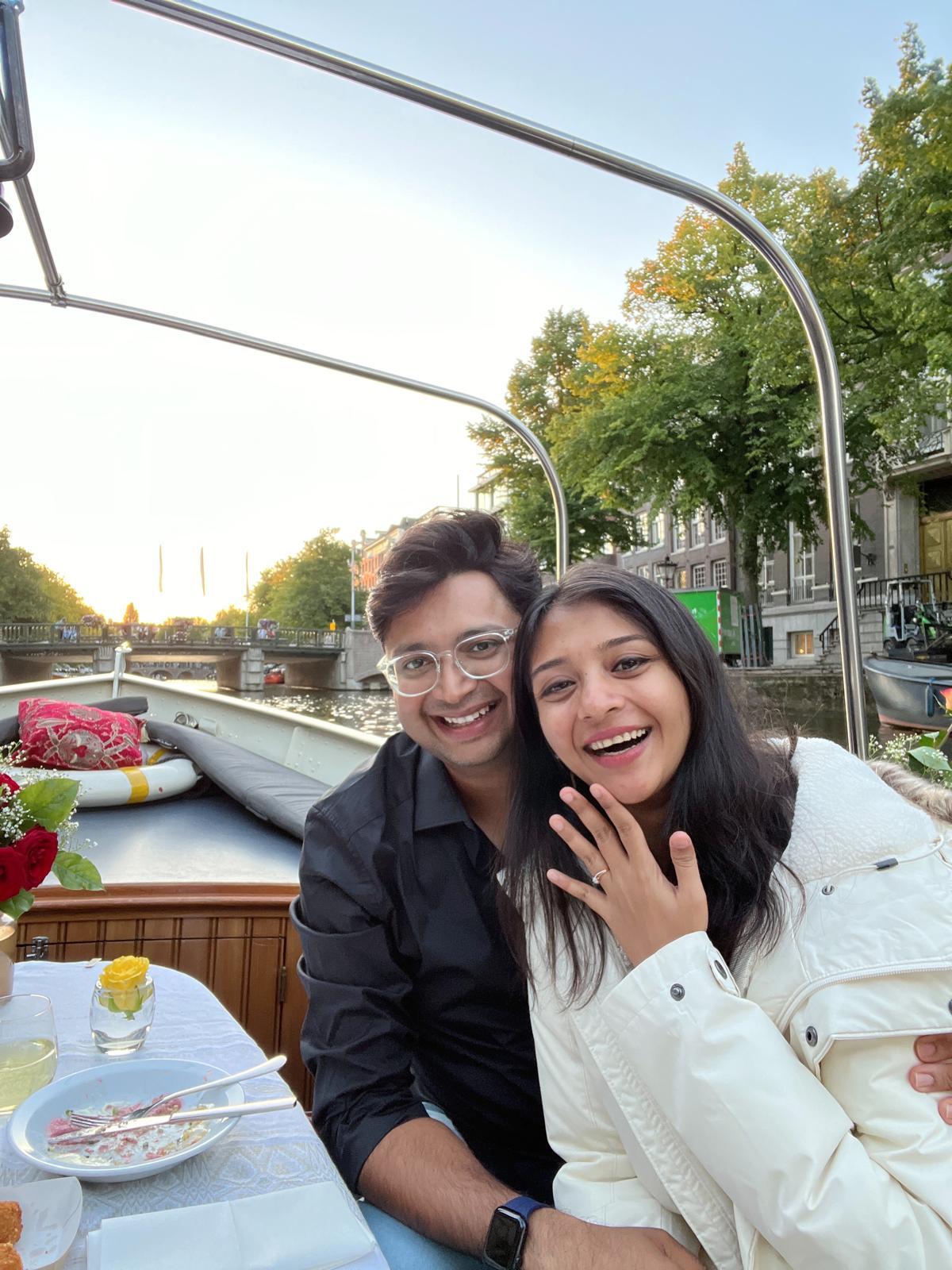 Priyam and Manish smiling together on a canal boat, with Priyam showing her ring